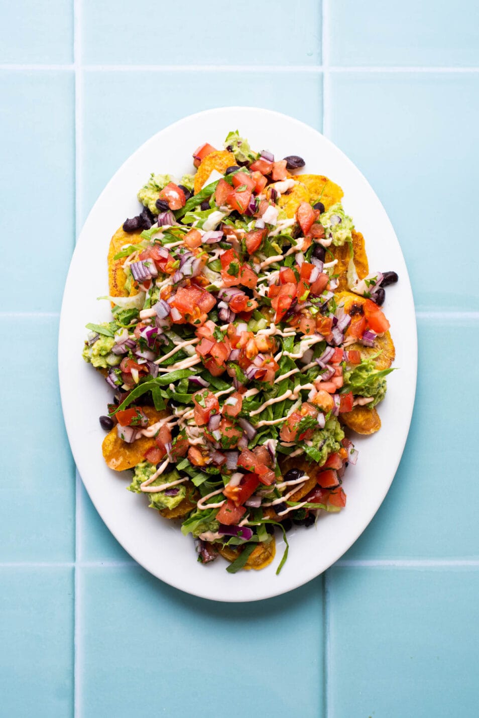 Vegan plantain nachos on a white oval platter with salsa, guacamole, and beans.
