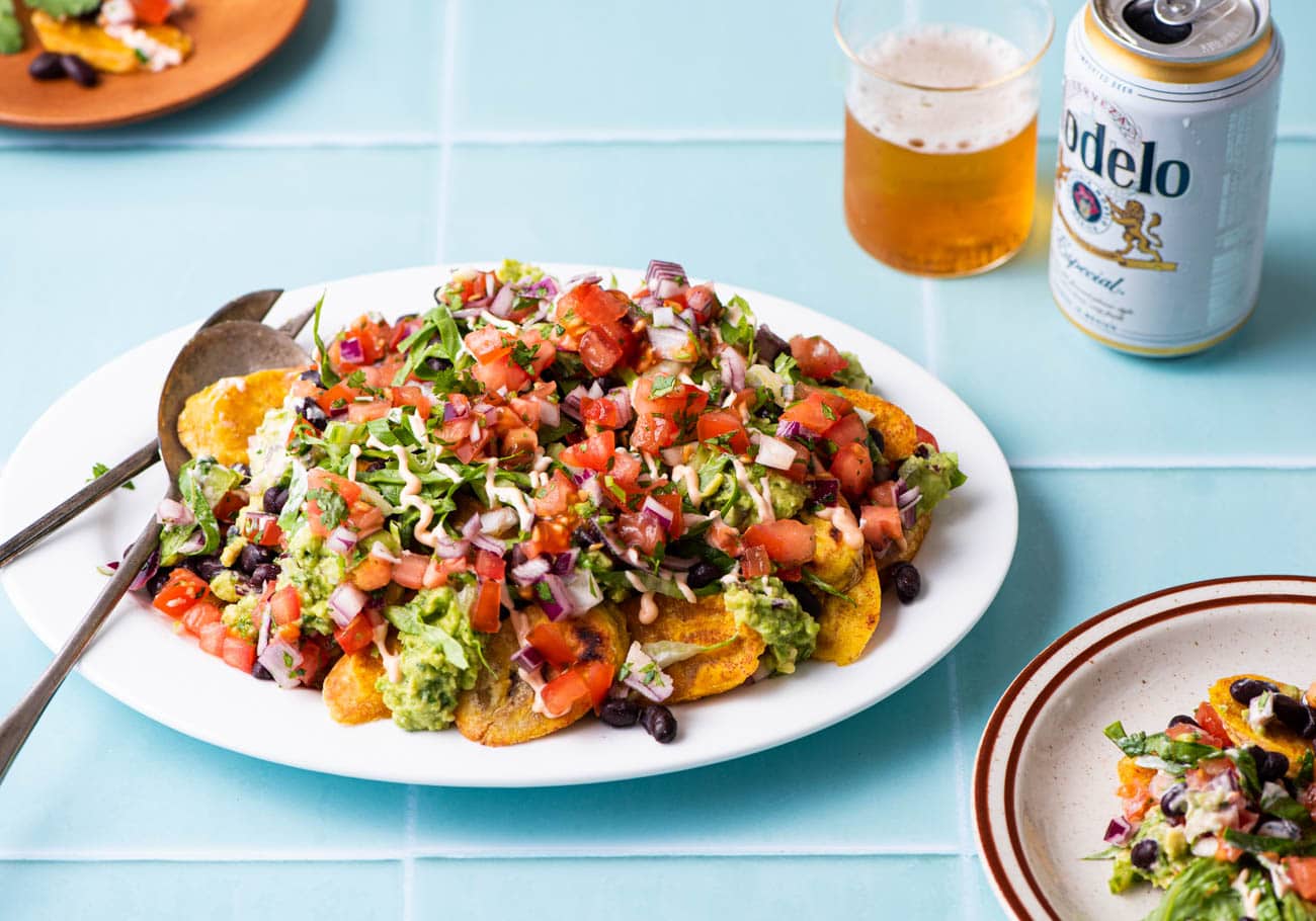 Plantain nachos on a white oval platter next to beer.