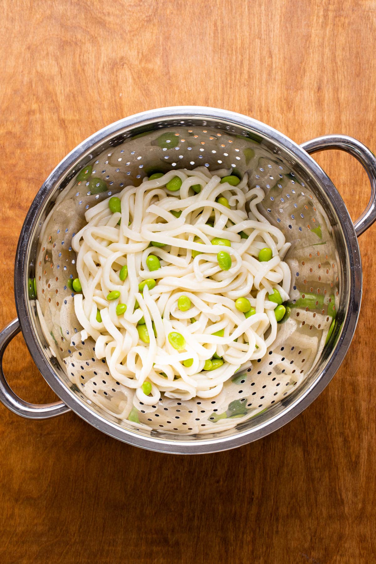 Drained udon noodles and edamame in a colander.