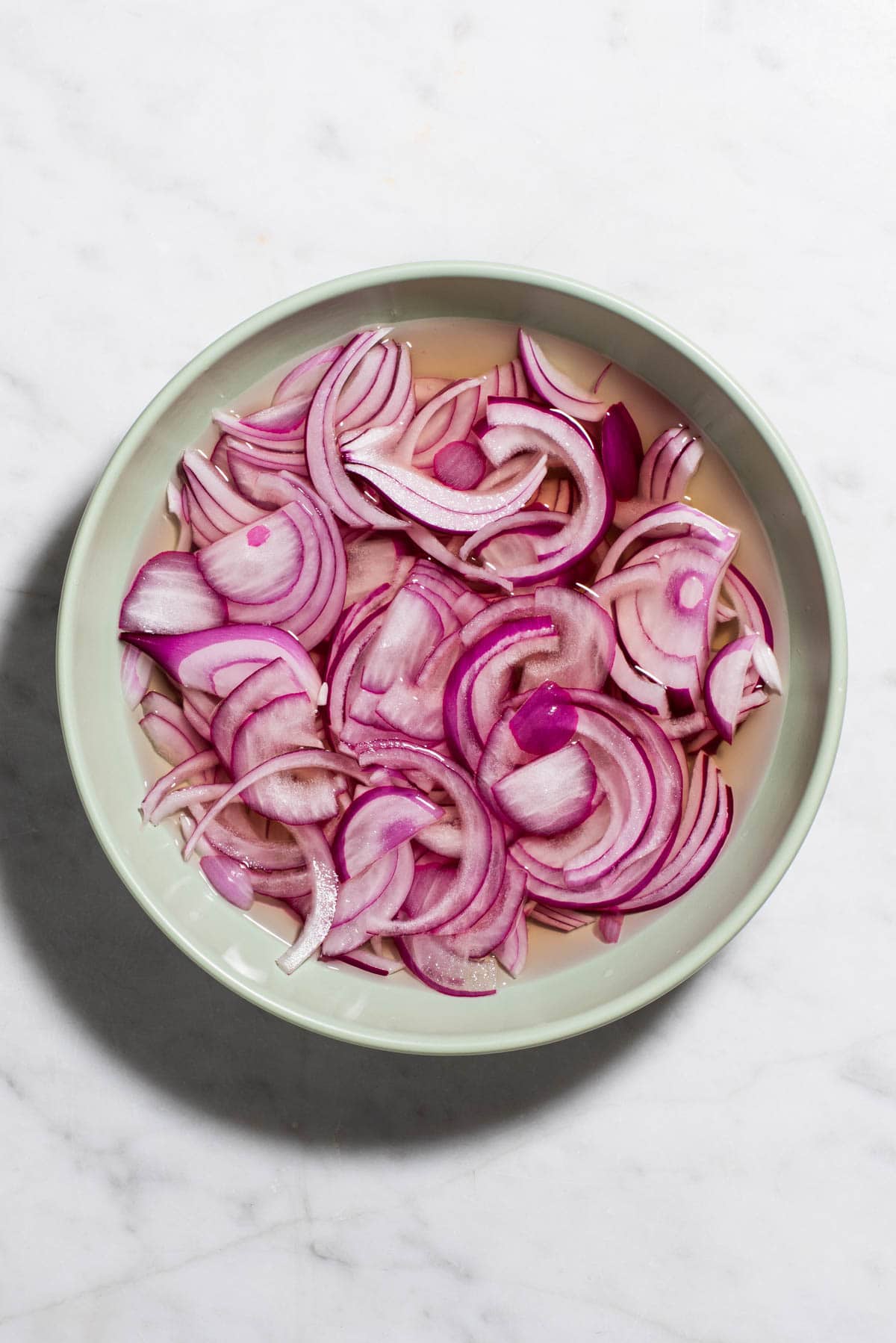 Homemade quick-pickled red onions in a blue bowl.