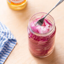 No-cook quick-pickled red onions in a jar on a wooden table.