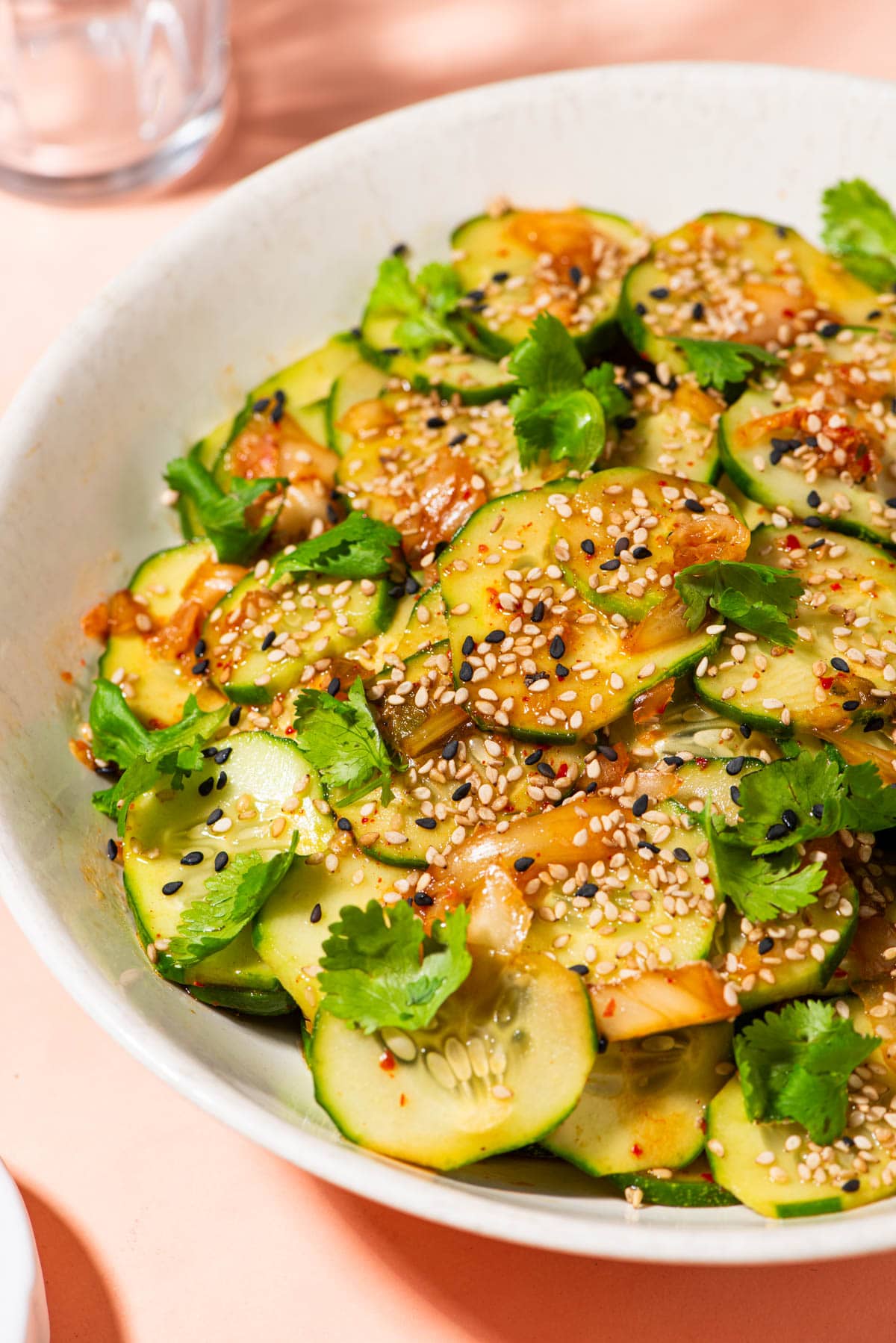Cucumber kimchi salad in a beige bowl, garnished with cilantro and sesame seeds.