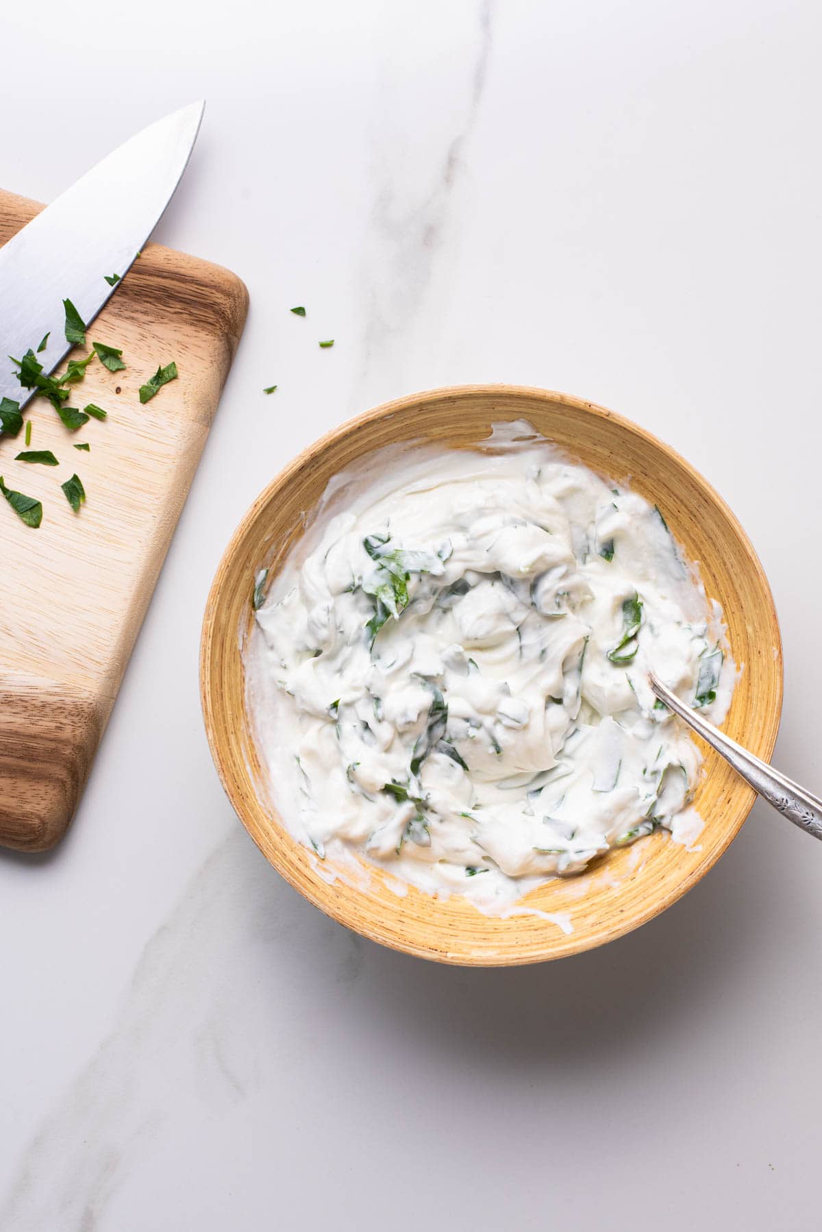 Spiced yogurt sauce with herbs in a wooden bowl.