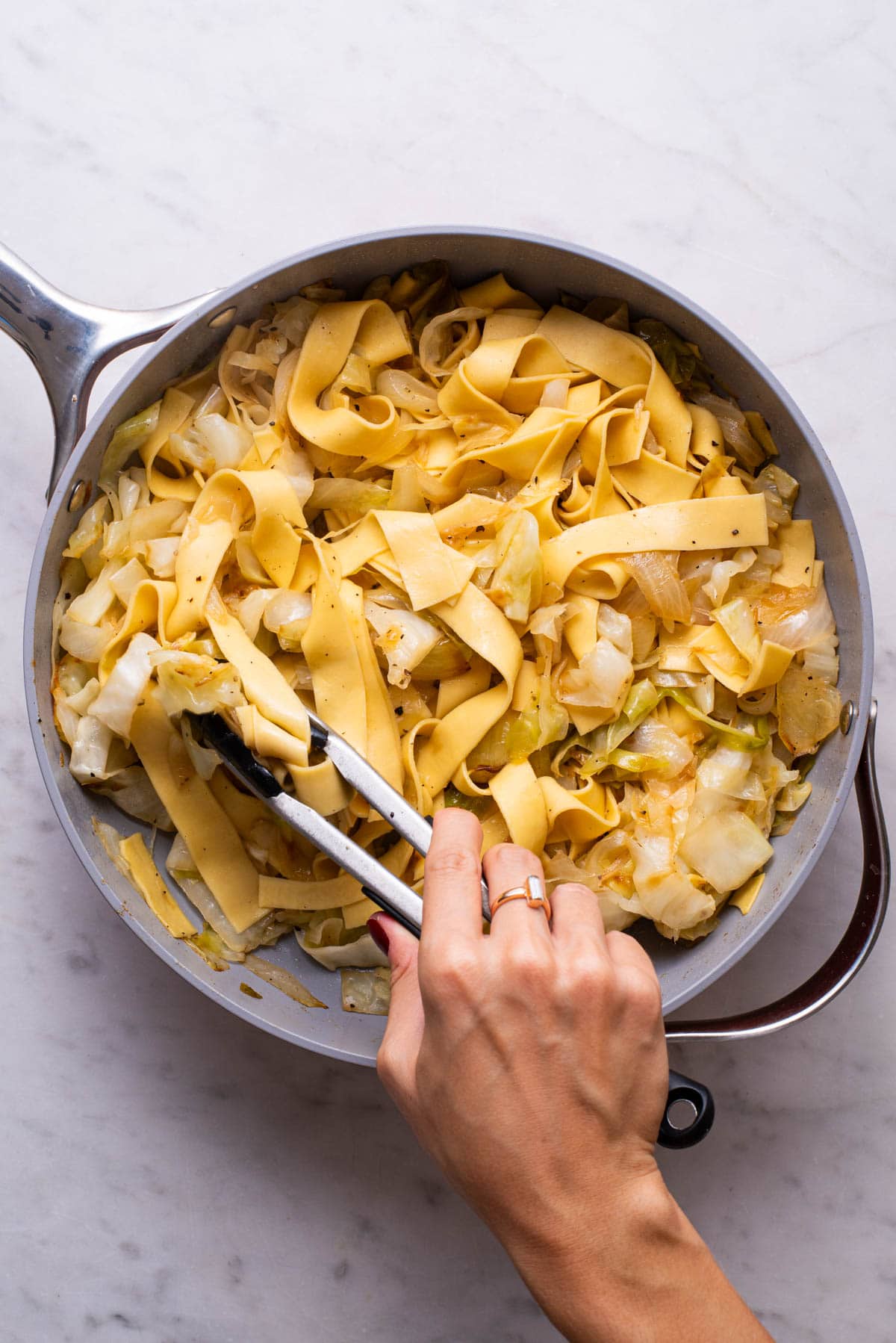 Tossing cooked pappardelle pasta through caramelized cabbage and onions.