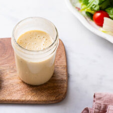 Creamy homemade salad dressing in a jar next to lettuce-tomato salad.