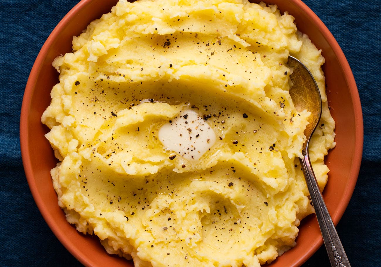 Vegan roasted garlic mashed potatoes in a terra cotta bowl with a pat of vegan butter melting on top.