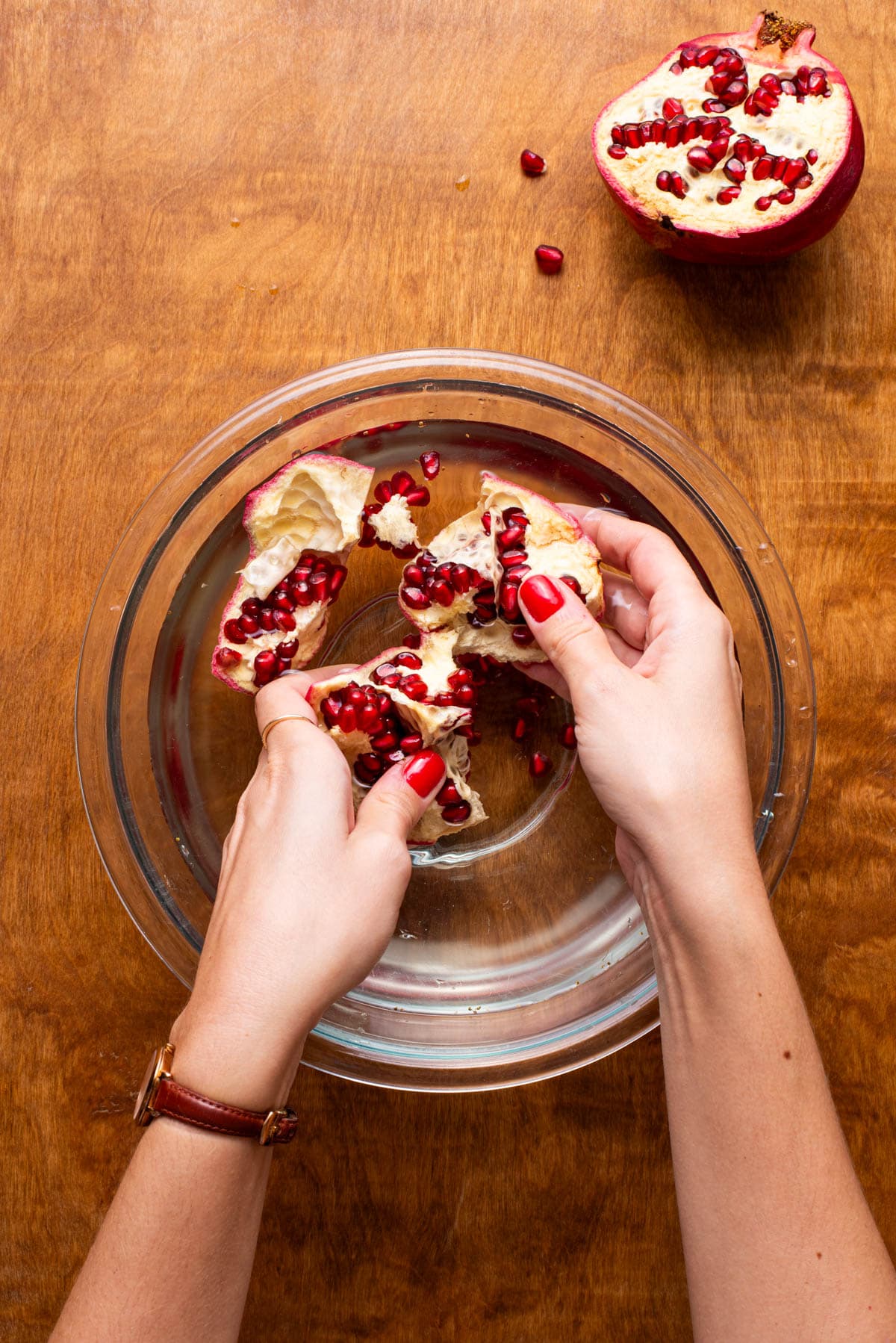 Woman's hands seeding pomegranate in a bowl of water.