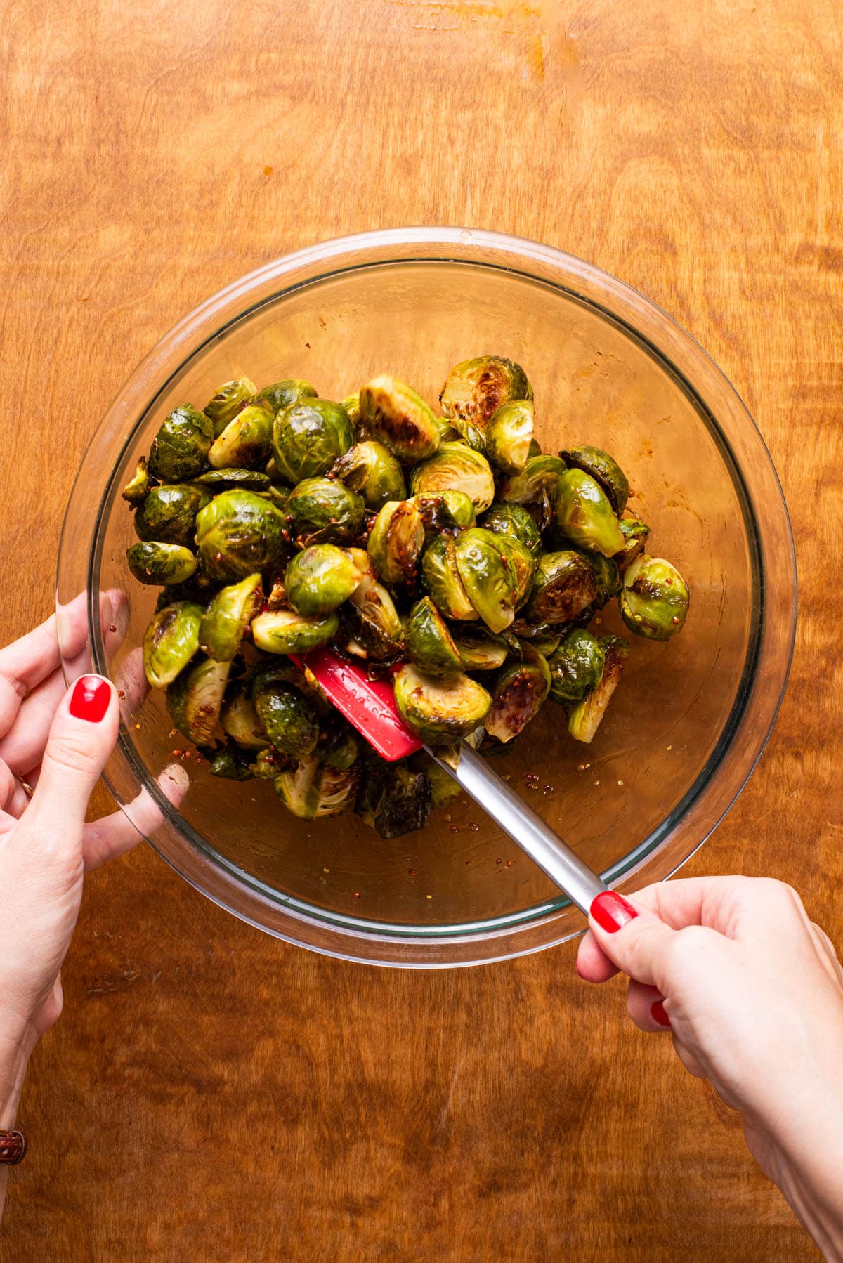 Coating roasted Brussels sprouts with balsamic maple glaze in a glass bowl.