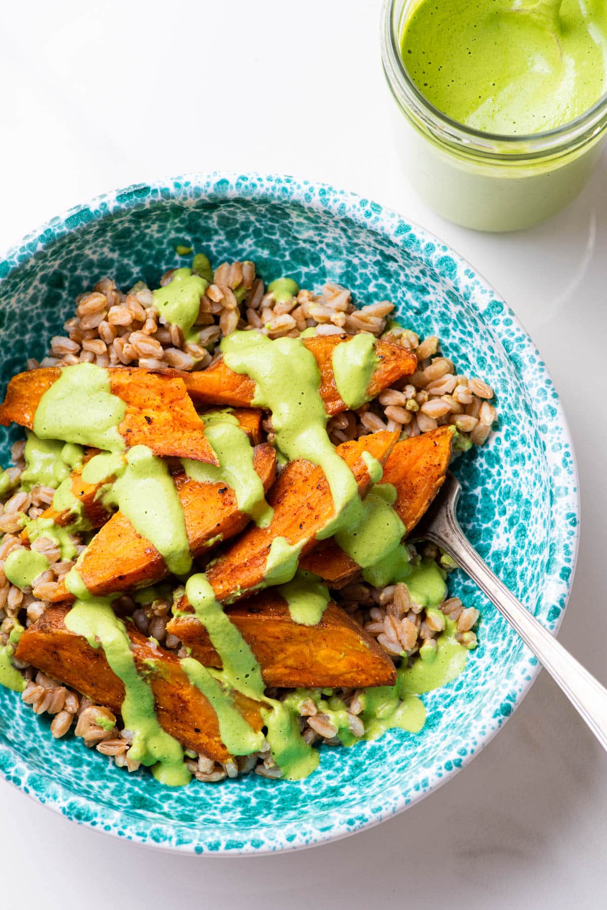 Vegan green goddess dressing drizzle on a bowl of farro and sweet potatoes.