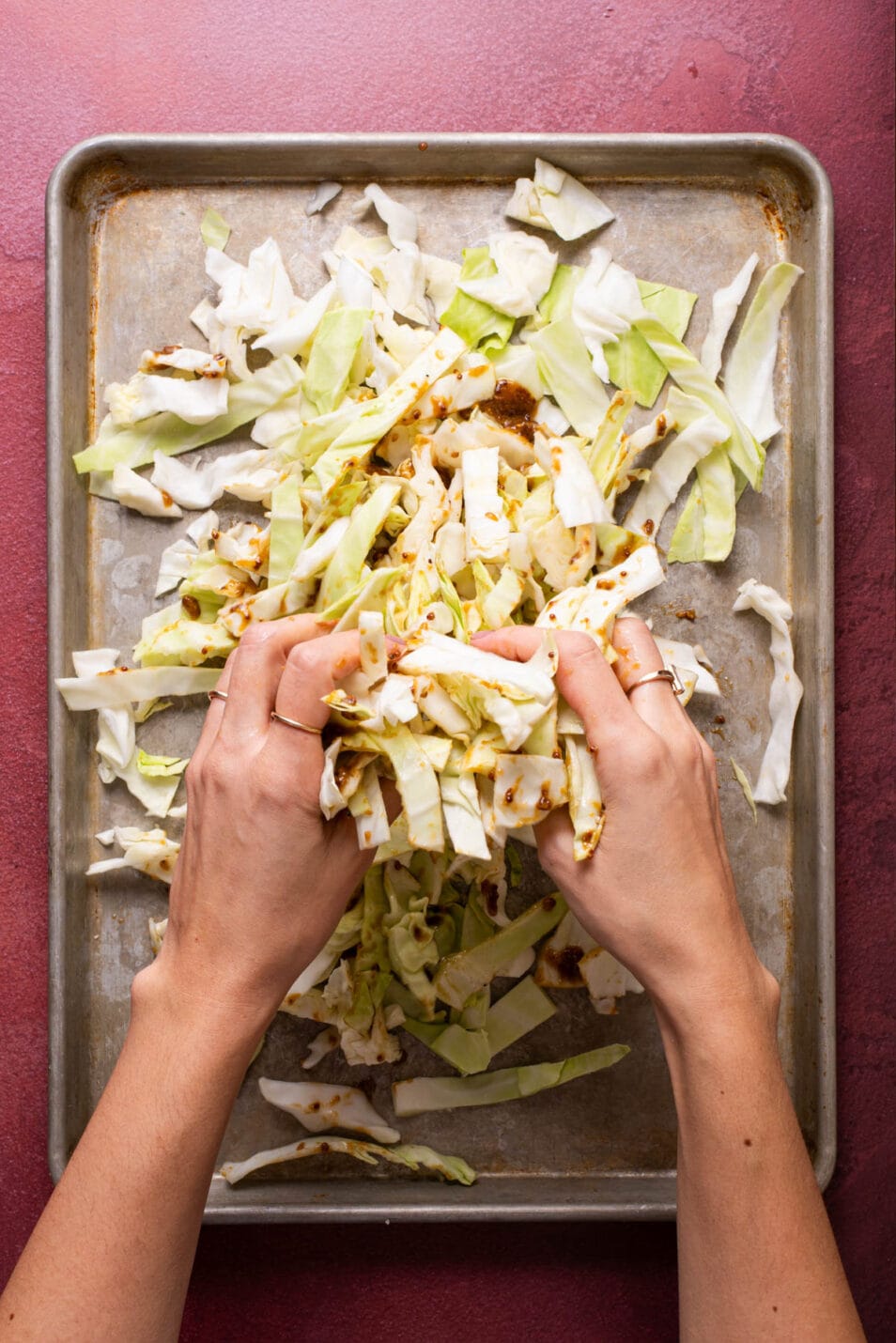Woman's hands tossing sliced green cabbage with miso glaze.