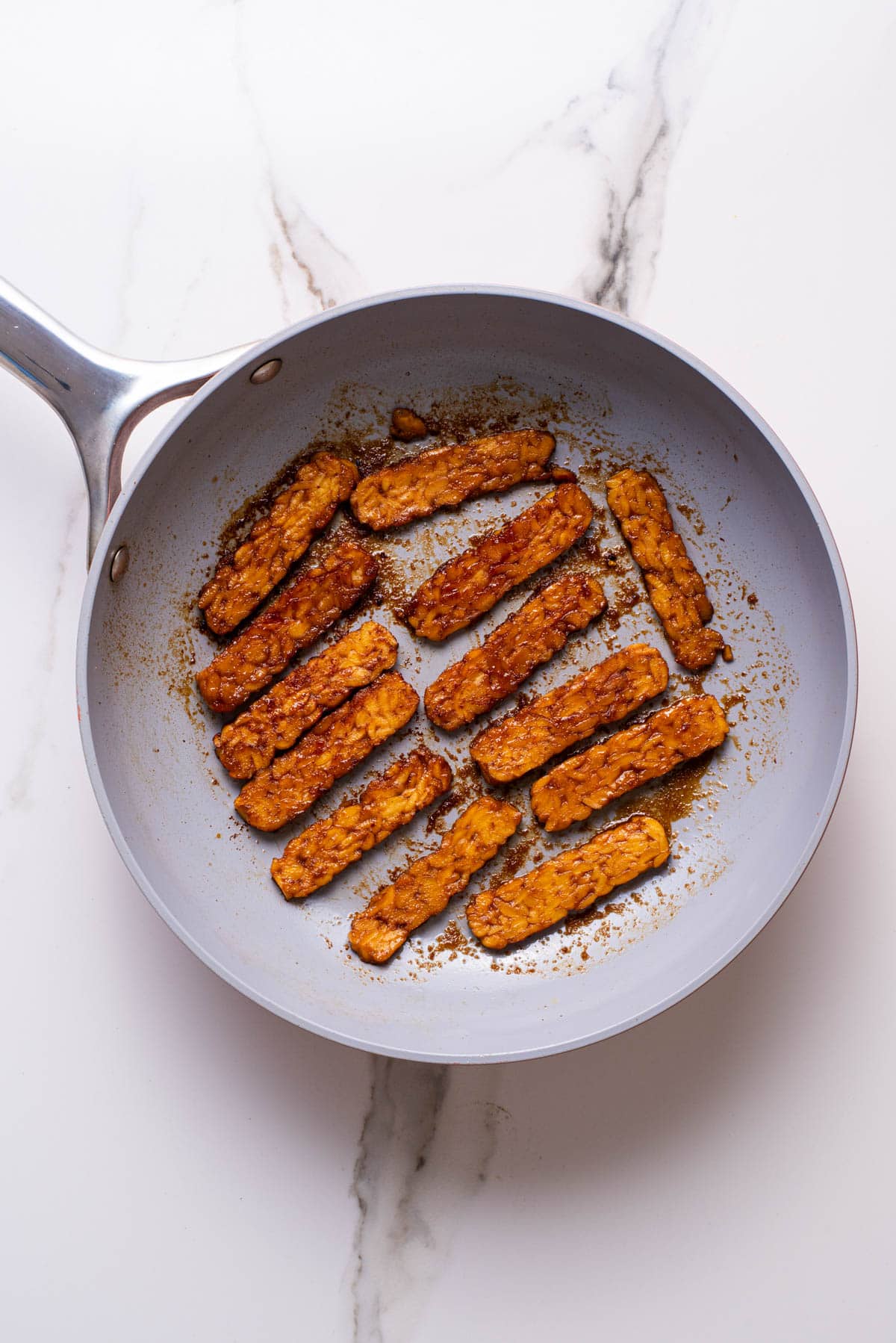 Marinated tempeh strips cooking in skillet.