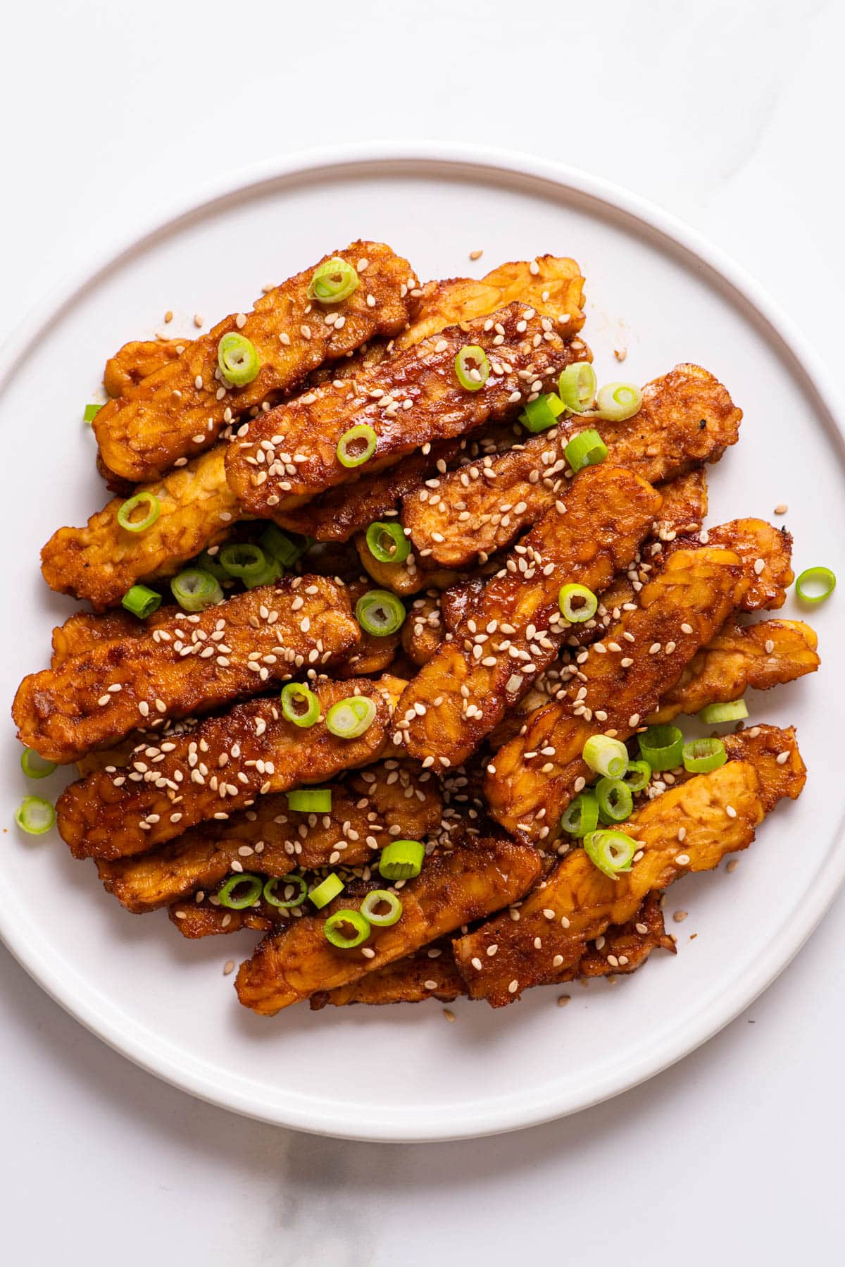 Baked marinated tempeh strips on white plate.
