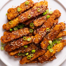 Baked marinated tempeh strips on white plate.