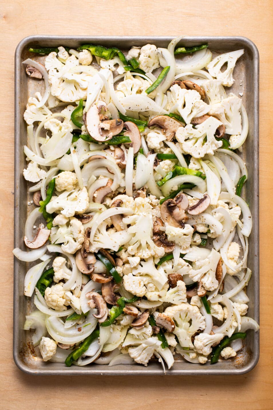 Chopped peppers, onions, mushrooms, and cauliflower on a baking sheet.