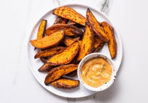 Air fryer sweet potato wedges on a white plate next to creamy dip.