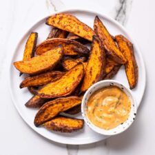 Air fryer sweet potato wedges on a white plate next to creamy dip.