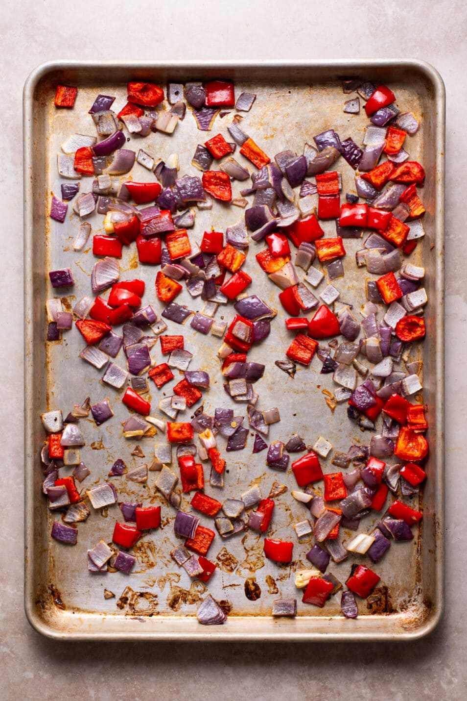Roasted cubed red onions and bell peppers on a baking sheet.