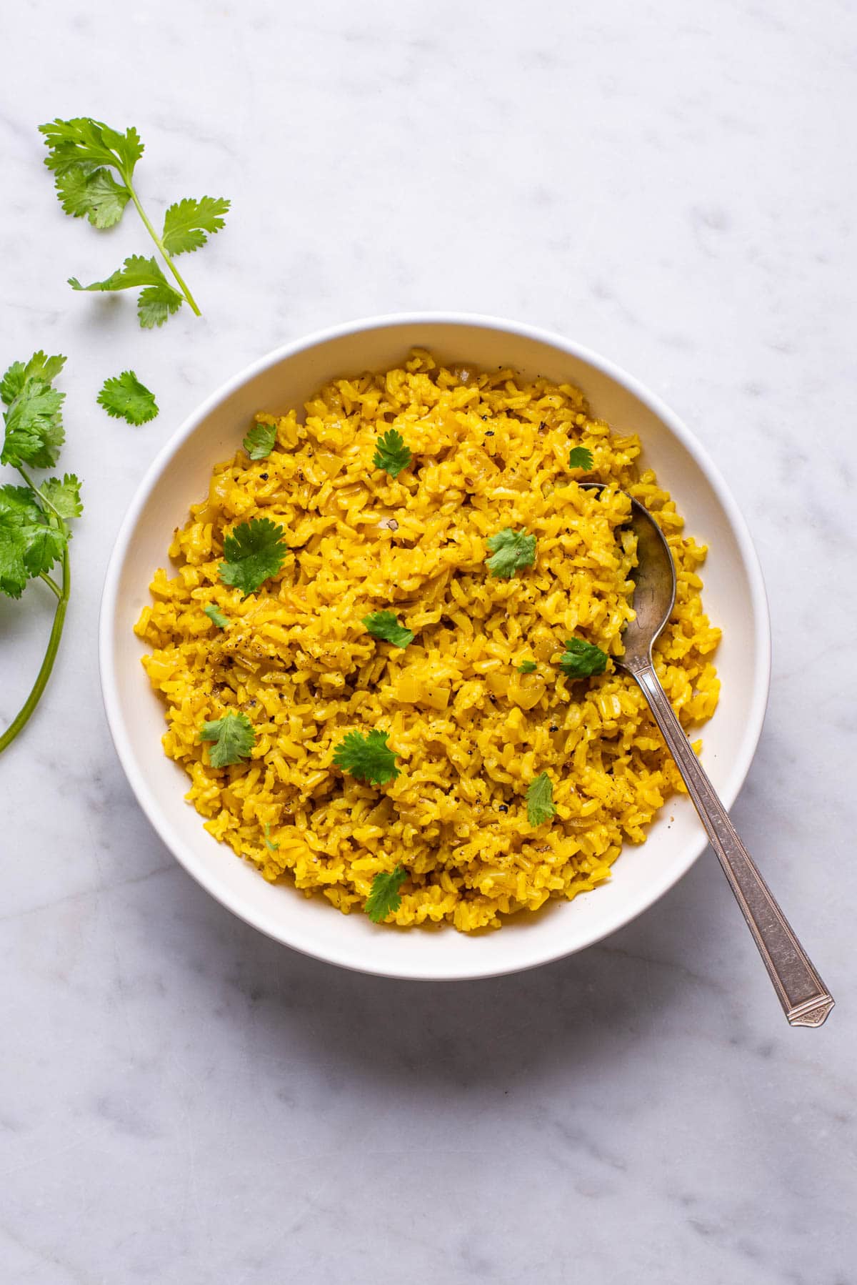 Turmeric rice in a white bowl garnished with cilantro.