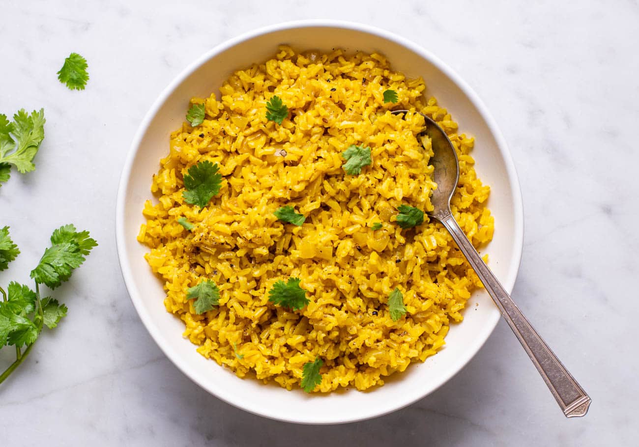 Turmeric rice in a white bowl garnished with cilantro.
