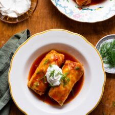 Vegetarian golubtsi (stuffed cabbage rolls) with tomato sauce, sour cream, and dill on a white plate.