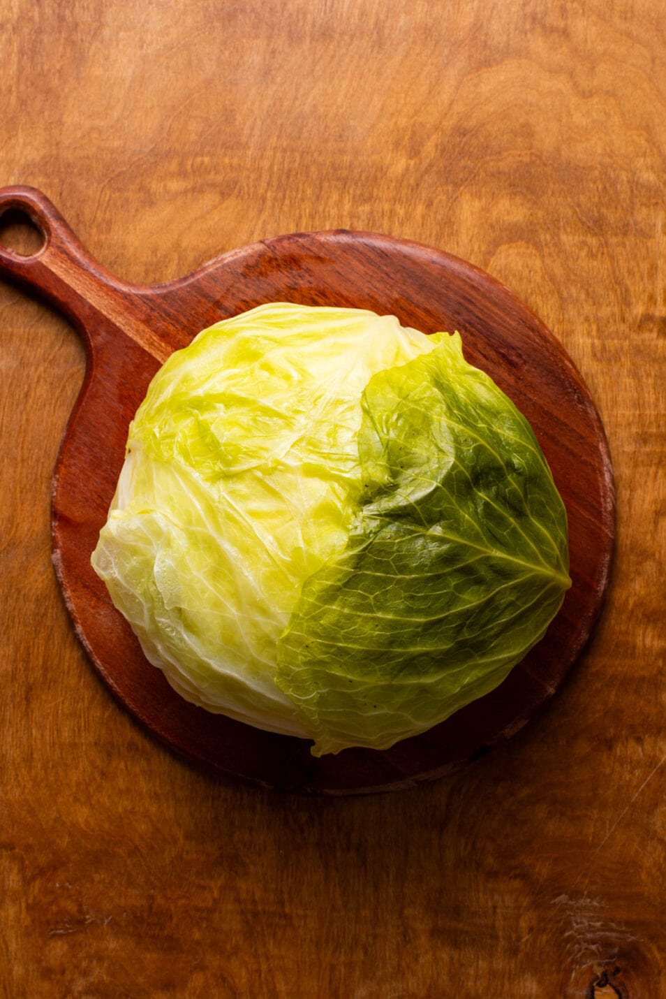 Whole boiled cabbage head cooling on a cutting board.