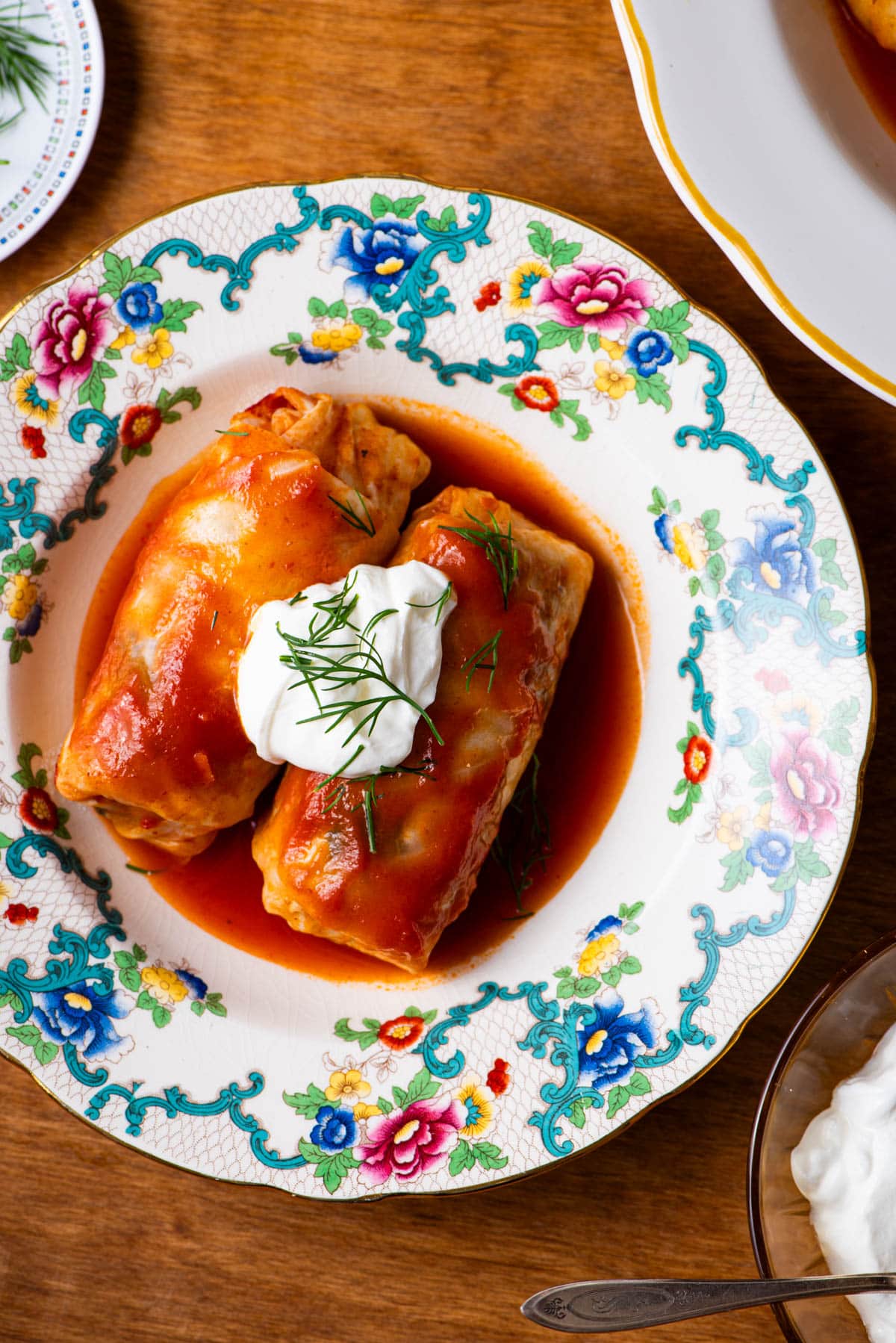 Vegetarian golubtsi (stuffed cabbage rolls) with tomato sauce, sour cream, and dill on a vintage plate.