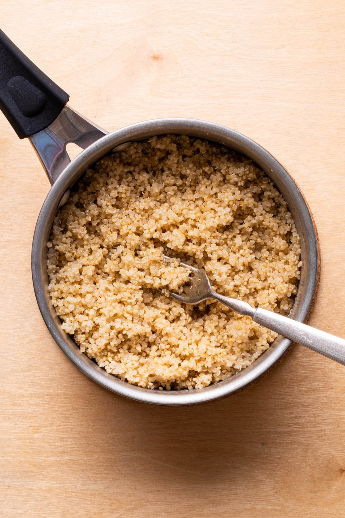 Cooked white quinoa in a pot, fluffed with a fork.