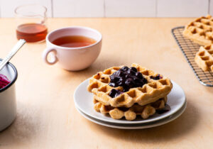 Waffles with blueberry sauce next to tea and maple syrup.