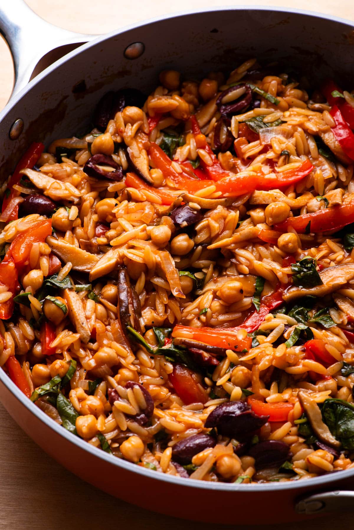 Baked Greek orzo in a skillet, with tomato sauce, olives, mushrooms, and chickpeas.