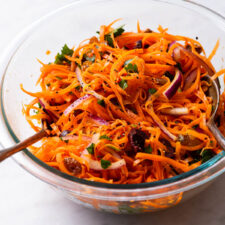 Shredded carrot salad with raisins and olives in a glass bowl.