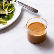 Sesame ginger dressing in small glass pourer next to salad.