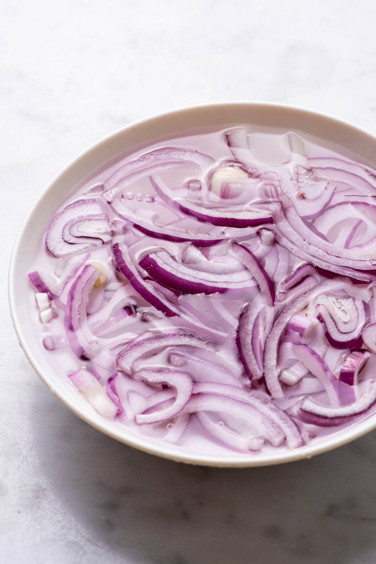 Raw red onions soaking in a bowl of water.