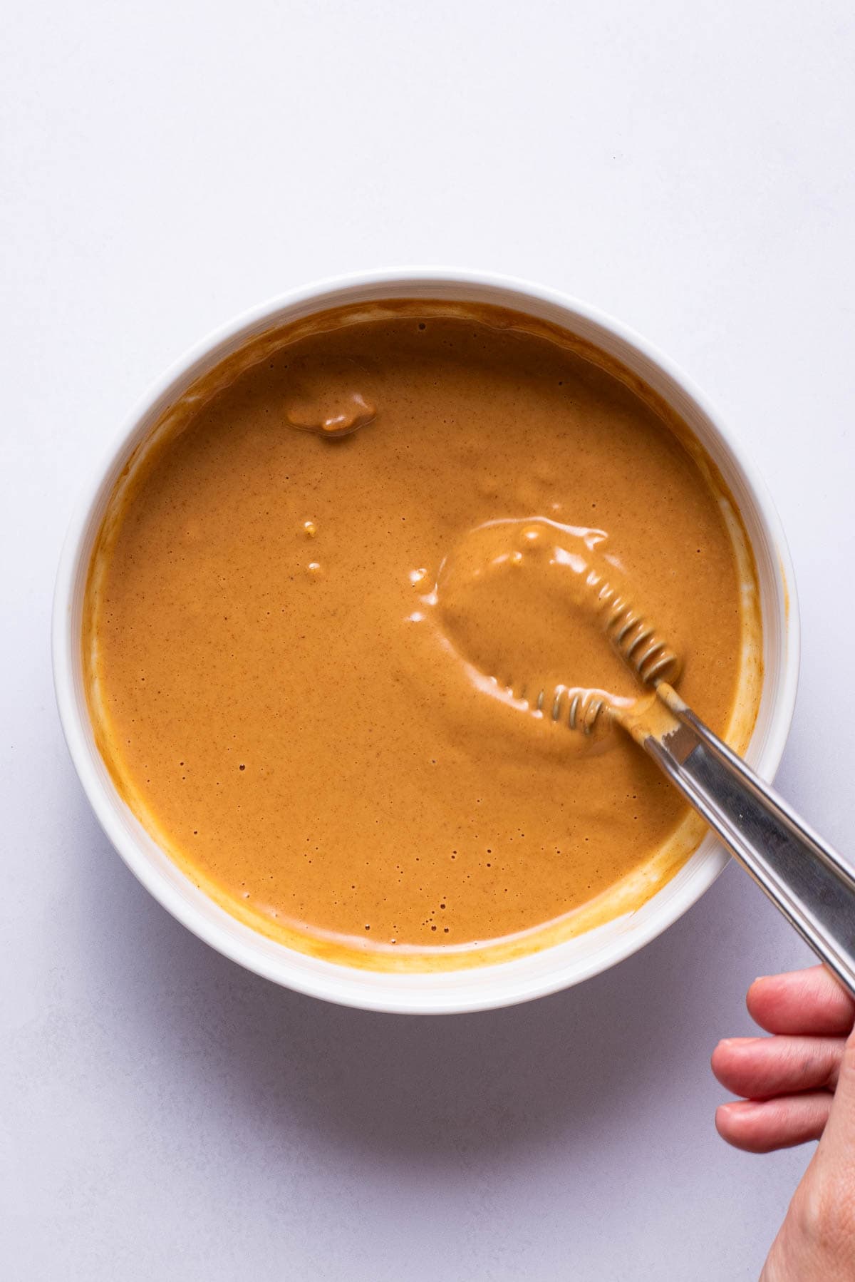 Homemade peanut butter sauce in a white bowl with a whisk.