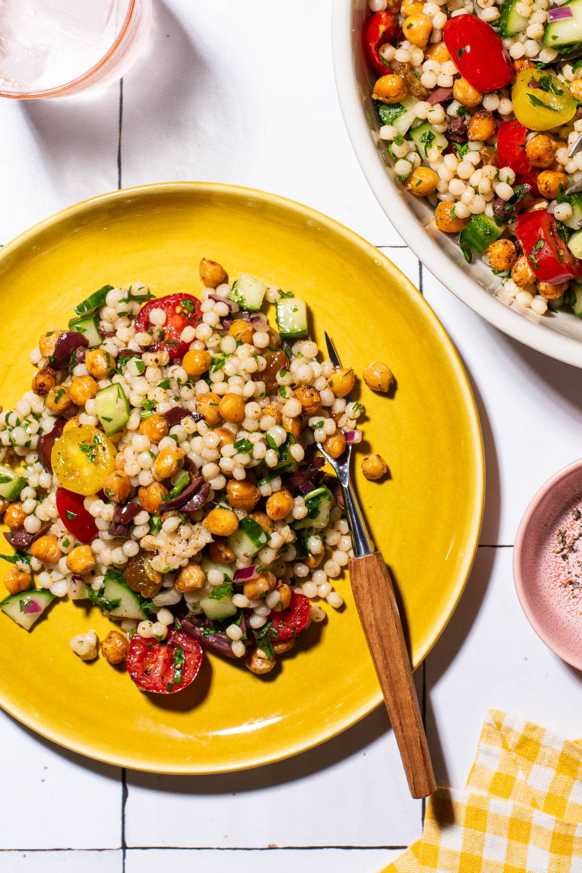 Summer pearl couscous salad with crispy chickpeas on a yellow plate.