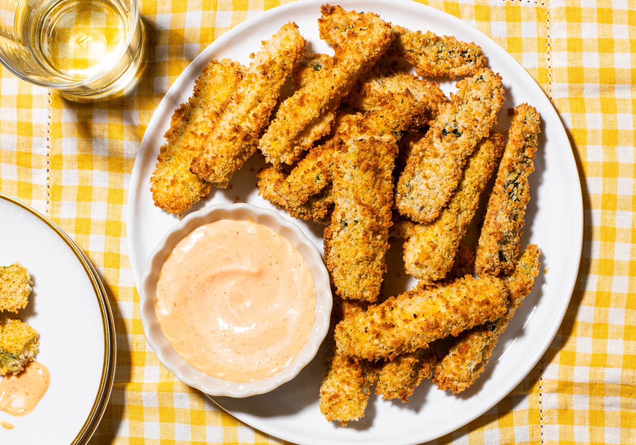 Air fryer zucchini fries next to spicy mayo on a white plate.