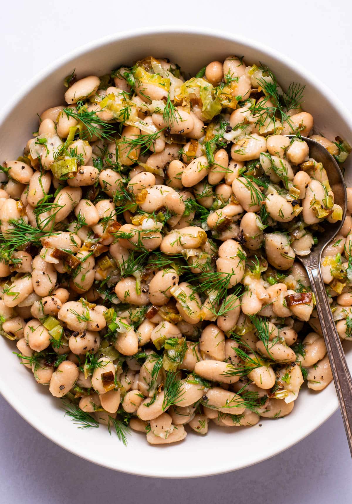 Herby cannellini bean salad in a white bowl.
