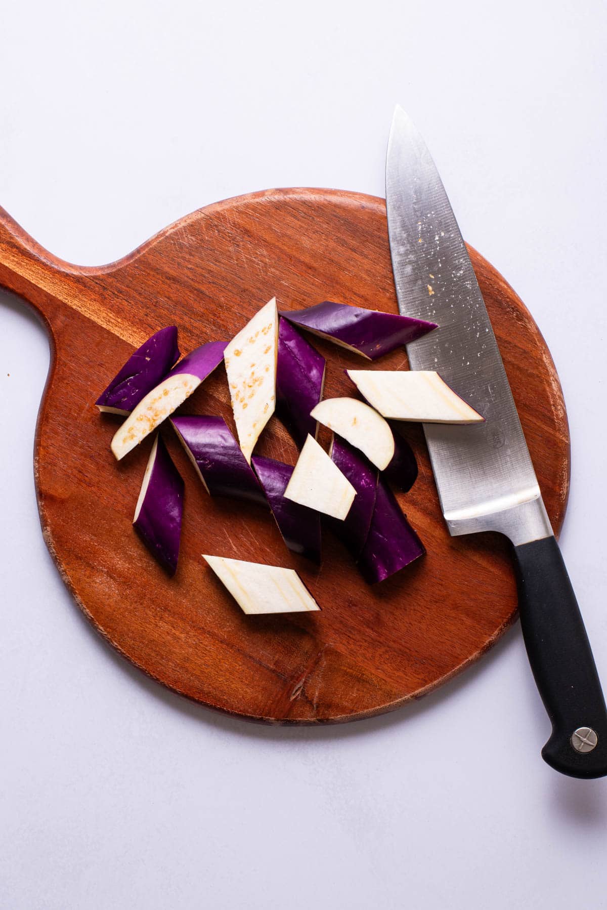 Chinese eggplant on a cutting board, chopped into chunks.
