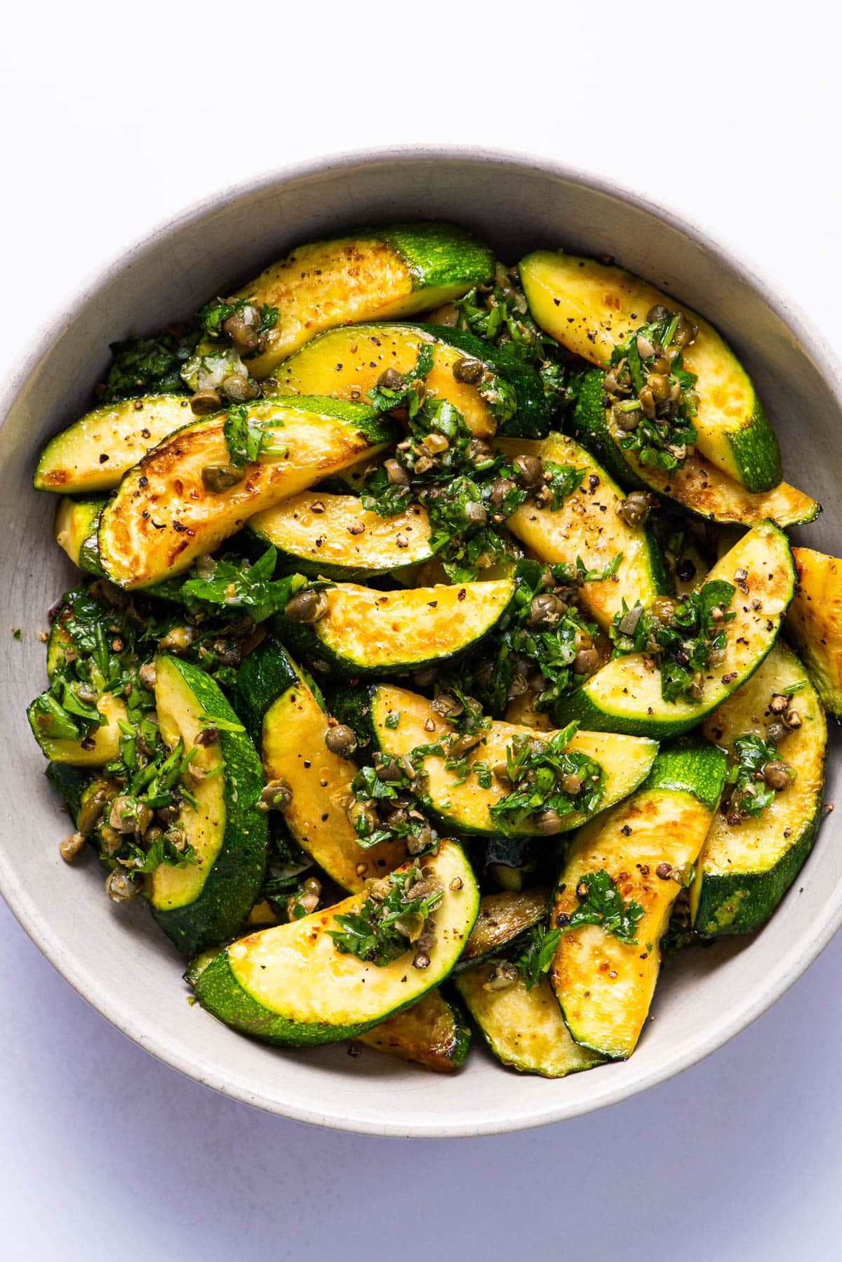 Pan-fried zucchini with caper relish in a bowl.