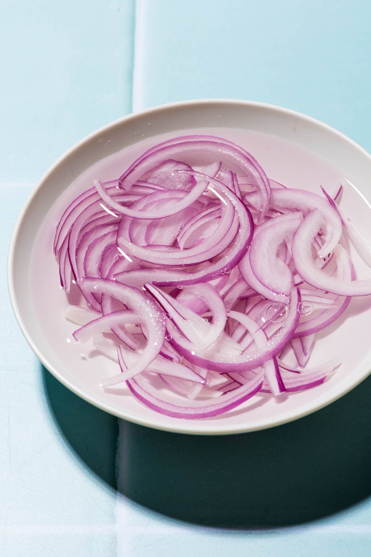 Sliced red onions soaking in a bowl of water.
