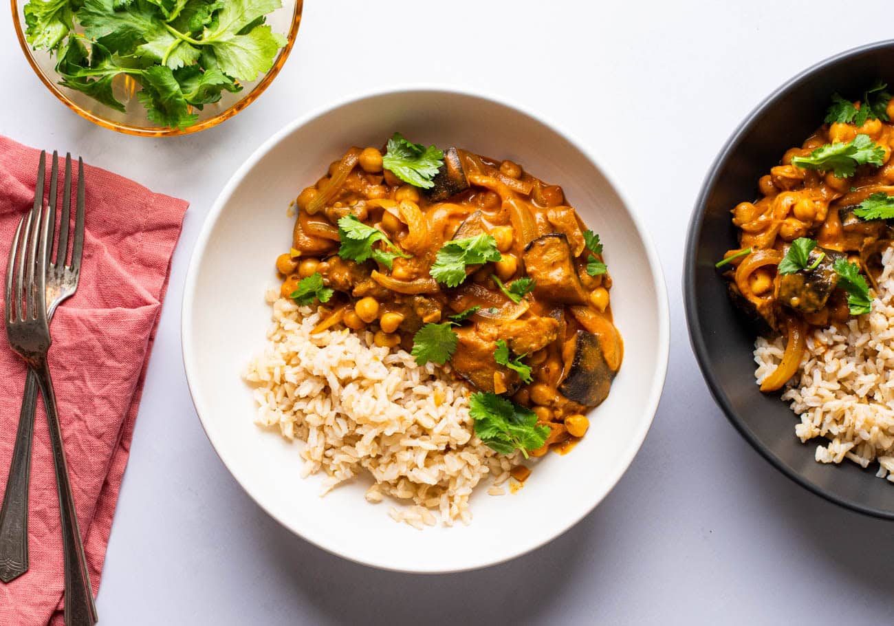 Two bowls of eggplant chickpea curry garnished with cilantro.