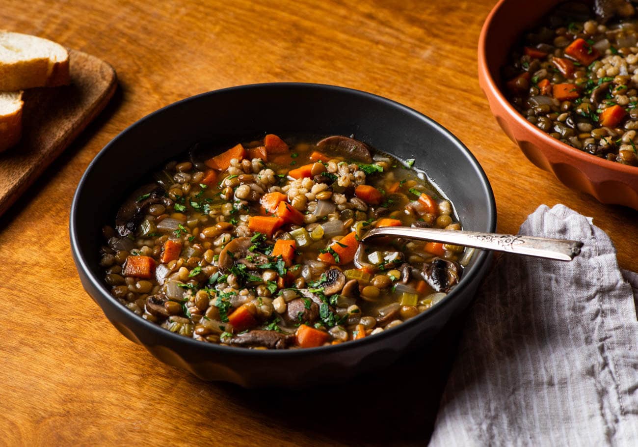 Lentil barley soup with mushrooms in a black bowl.